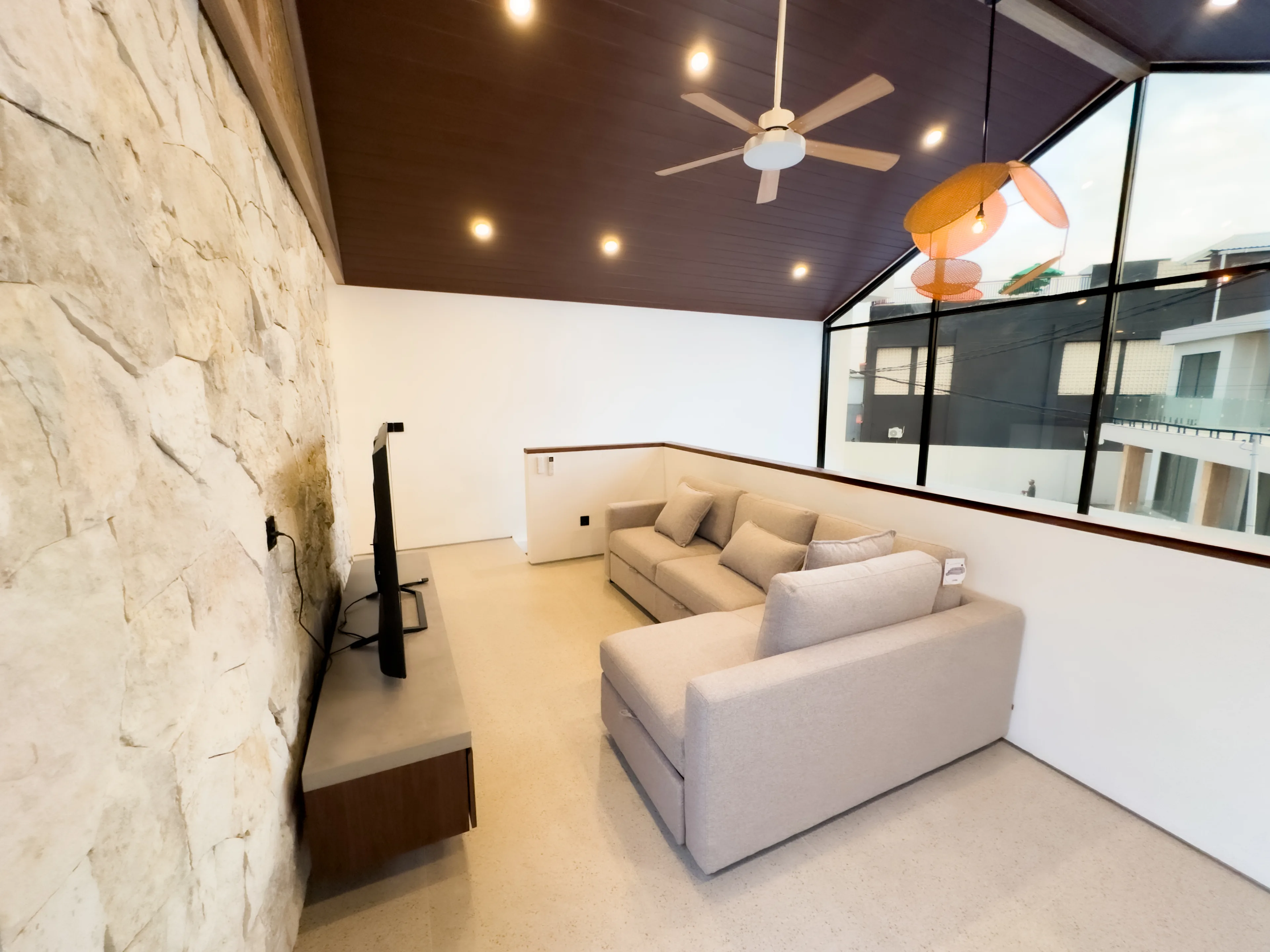 Living area of a delivered villa, with a stone feature wall under the timber-lined pitched ceiling