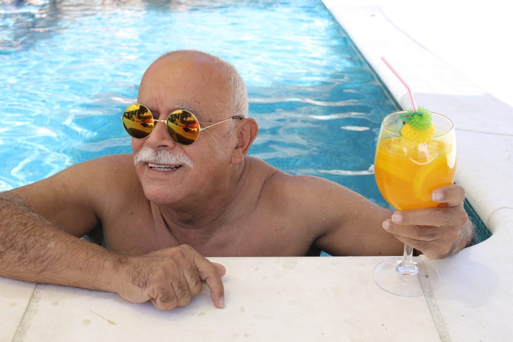 Senior man drinking cocktail in swimming pool.